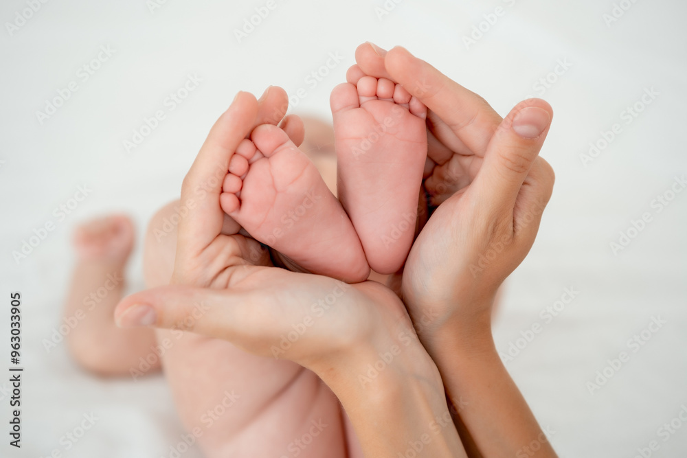 mom's hands hold the legs of a newborn baby, legs in focus, pink baby heels mom's hands hold the legs of a newborn baby, legs in focus, pink baby heels