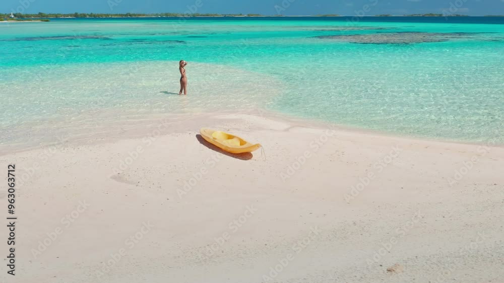Woman is wading in the crystal-clear turquoise water of a tropical beach, with a yellow kayak resting on the white sand nearby Woman is wading in the crystal-clear turquoise water of a tropical beach, with a yellow kayak resting on the white sand nearby