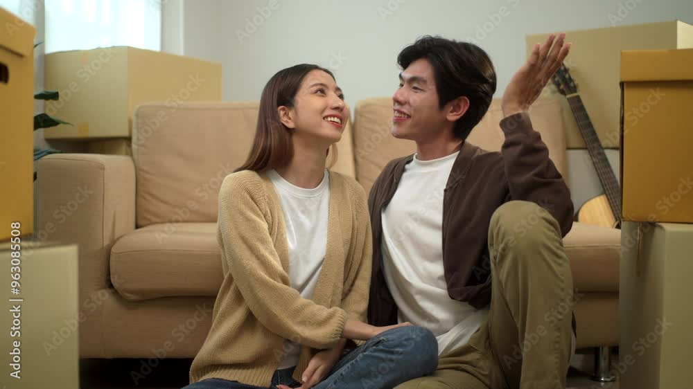 Young happy homeowner holding hands and smiling to each other after moving to new house, cheerful couple pleasant in moving day in new real estate, relocating new apartment concept.
