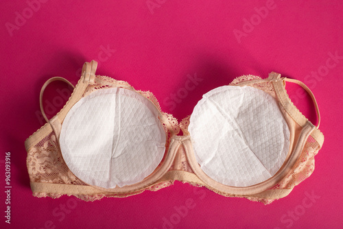 Women's bra with liners against the flow of milk from the breast of a nursing woman on a pink background. photo