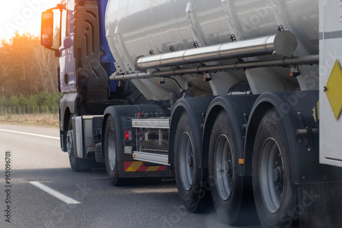 A tanker semi-trailer truck transports a dangerous cargo of gasoline, diesel fuel and petroleum products on the road against the backdrop of the sun. Cargo hazard class. Copy space for text photo