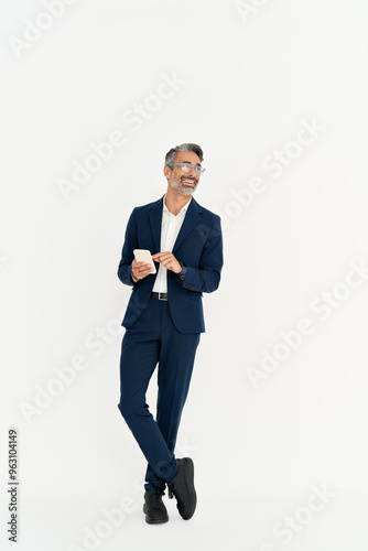 Happy business man of middle age wearing suit using phone standing isolated on white background. Busy mature businessman with smartphone in hands looking away advertising mobile services. Full body.