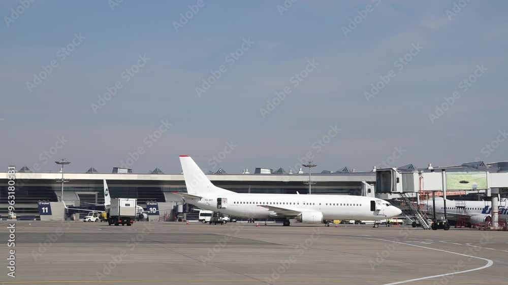 Airplanes parked at the terminal with control tower and airport infrastructure during daytime at a busy international airport Airplanes parked at the terminal with control tower and airport infrastructure during daytime at a busy international airport