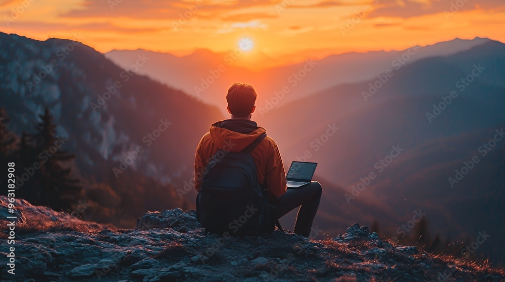 Obraz premium A lone hiker sits on a mountaintop at sunset, working on a laptop.