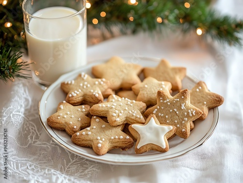 a plate of freshly baked Christmas cookies in festive shapes like stars and trees, with a glass of milk, set on a white tablecloth photo