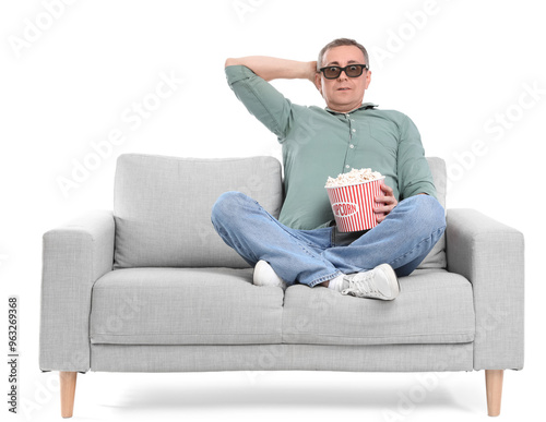 Scared mature man in 3D glasses with popcorn watching movie on sofa against white background