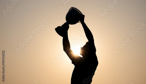 Silhouette of a person holding a trophy up high against the setting sun.