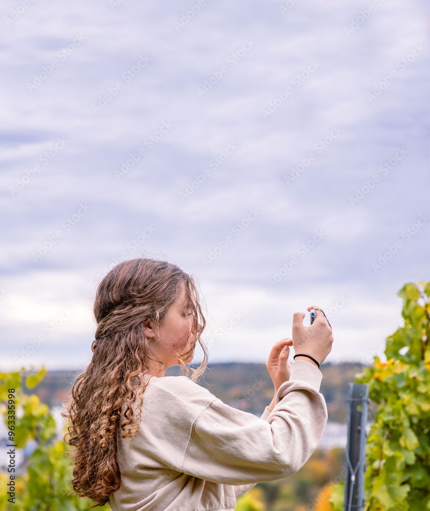 A young woman with long curly hair capturing scenic vineyard landscape views with her smartphone. Teenager blogger girl photographing autumn nature with her phone. Copy space
A young woman with long curly hair capturing scenic vineyard landscape views with her smartphone. Teenager blogger girl photographing autumn nature with her phone. Copy space