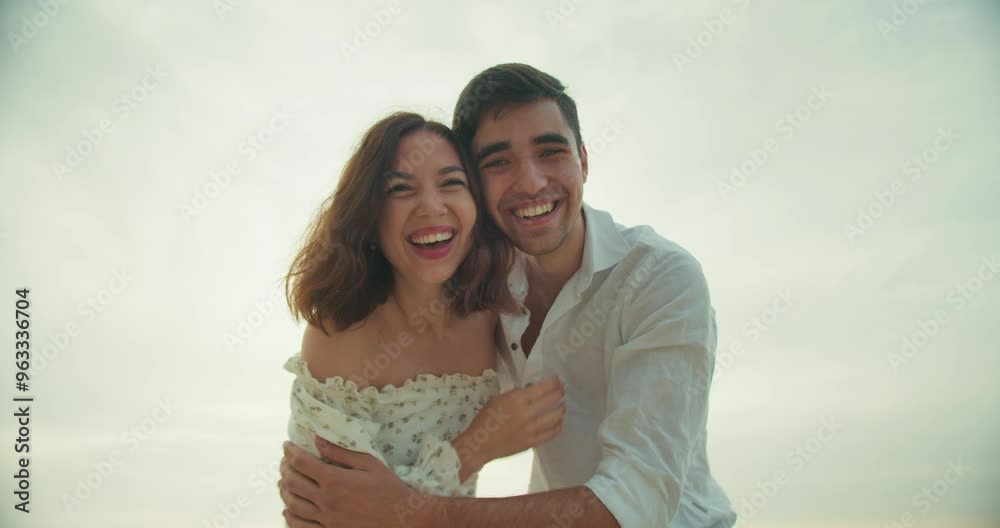 Portrait of a cheerful and happy guy who together with his happy girlfriend looks at the camera and fools around on the beach in the summer morning Portrait of a cheerful and happy guy who together with his happy girlfriend looks at the camera and fools around on the beach in the summer morning