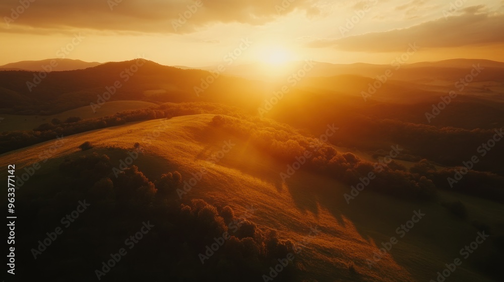 Naklejka premium Golden Sunset over Rolling Hills and Forested Landscape