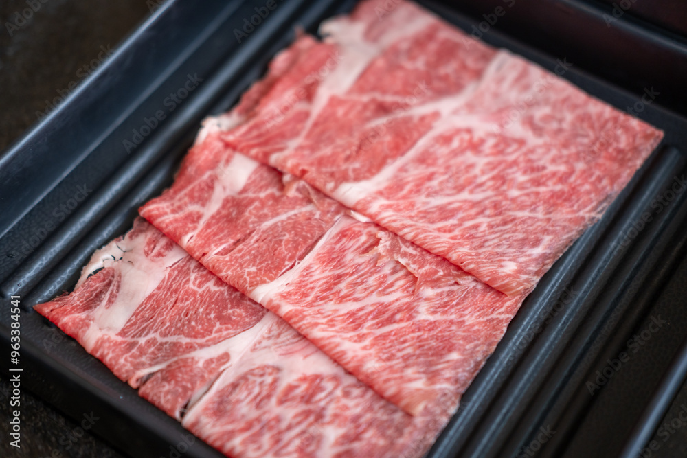 A close-up shot of sliced raw meat, arranged on a plate, ready to be cooked in a hot pot A close-up shot of sliced raw meat, arranged on a plate, ready to be cooked in a hot pot
