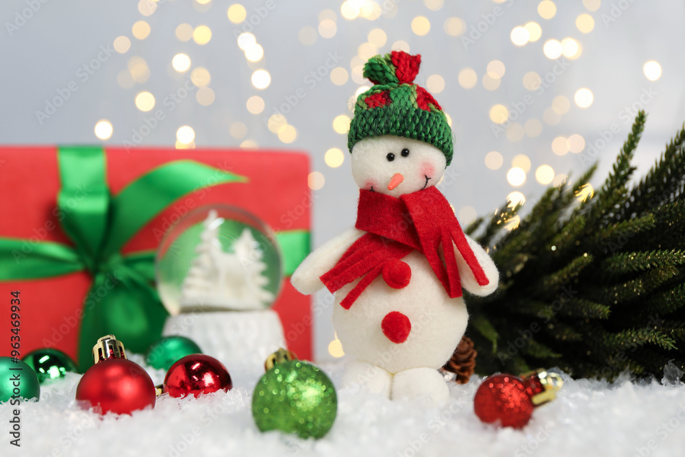 Funny snowman figure and other Christmas decor on artificial snow against blurred lights Funny snowman figure and other Christmas decor on artificial snow against blurred lights