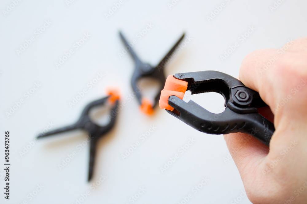Caucasian hand holding a plastic spring clamp over white background. Heavy duty clips for crafts, backdrop stand, woodworking, electrical installation, photo studios, industrial fixing grip tool. Caucasian hand holding a plastic spring clamp over white background. Heavy duty clips for crafts, backdrop stand, woodworking, electrical installation, photo studios, industrial fixing grip tool.