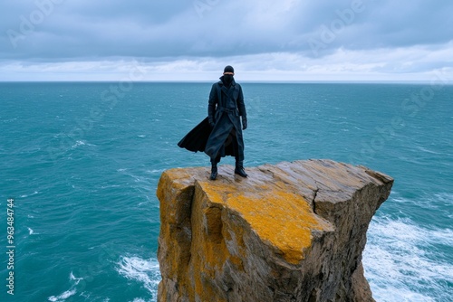 Masked man standing at the edge of a cliff his long coat flapping in the wind, gazing into the stormy sea below photo