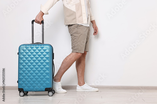 Man with suitcase near light wall walking indoors, closeup. Space for text