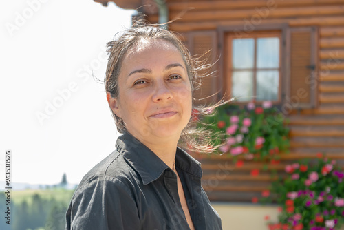 Street portrait of a dark-haired joyful woman 40-45 years old on the background of a wooden house with flowers. photo