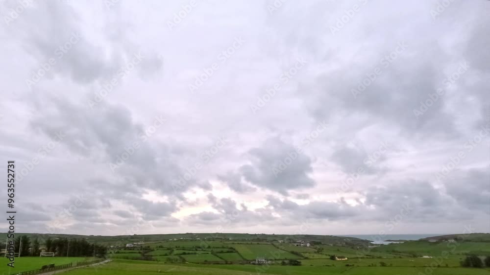 A view of a rolling green countryside with a few scattered farmhouses. There is a dirt road winding through the landscape with a fence alongside it. The sky is mostly cloudy. A view of a rolling green countryside with a few scattered farmhouses. There is a dirt road winding through the landscape with a fence alongside it. The sky is mostly cloudy.