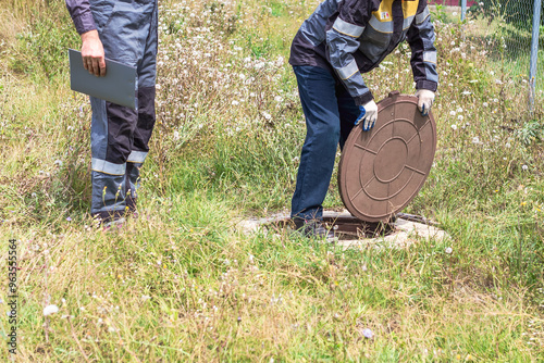 Plumbers work near an open well. The men opened the manhole cover to repair the pipes photo