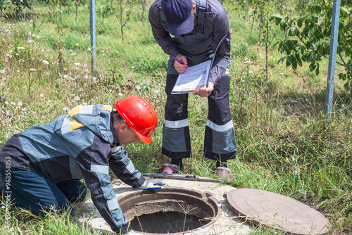 Plumbers working near an open well. A man inspects a water well, takes meter readings