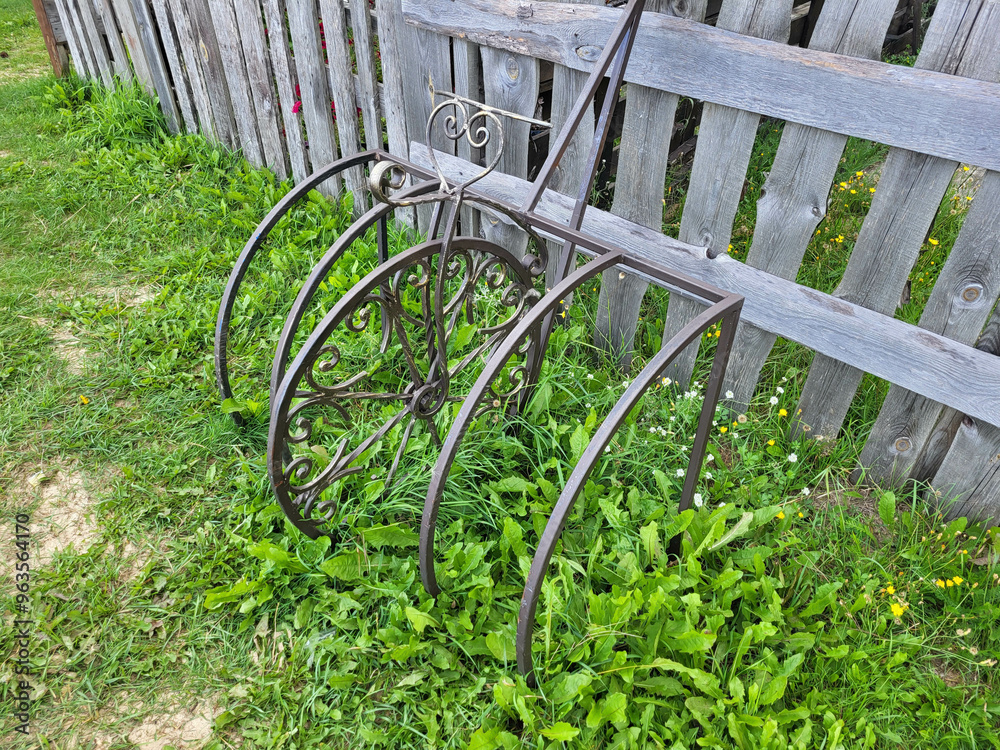 Forged bike rack near a wooden fence on the green grass.