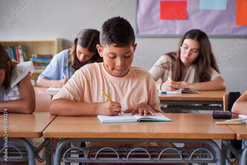 Front view of a group of preteens in primary school concentrated studying in the classroom doing homework writing on a notebook. Copy space image.