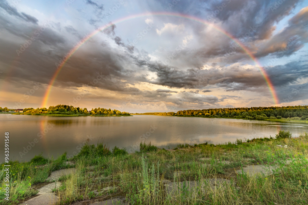 A rainbow is seen over a lake with a cloudy sky in the background A rainbow is seen over a lake with a cloudy sky in the background