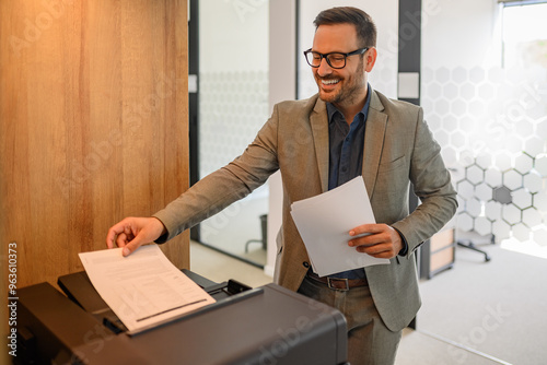 Obraz na plátně Portrait of smiling male printer smiling and putting sheet of paper into photoco