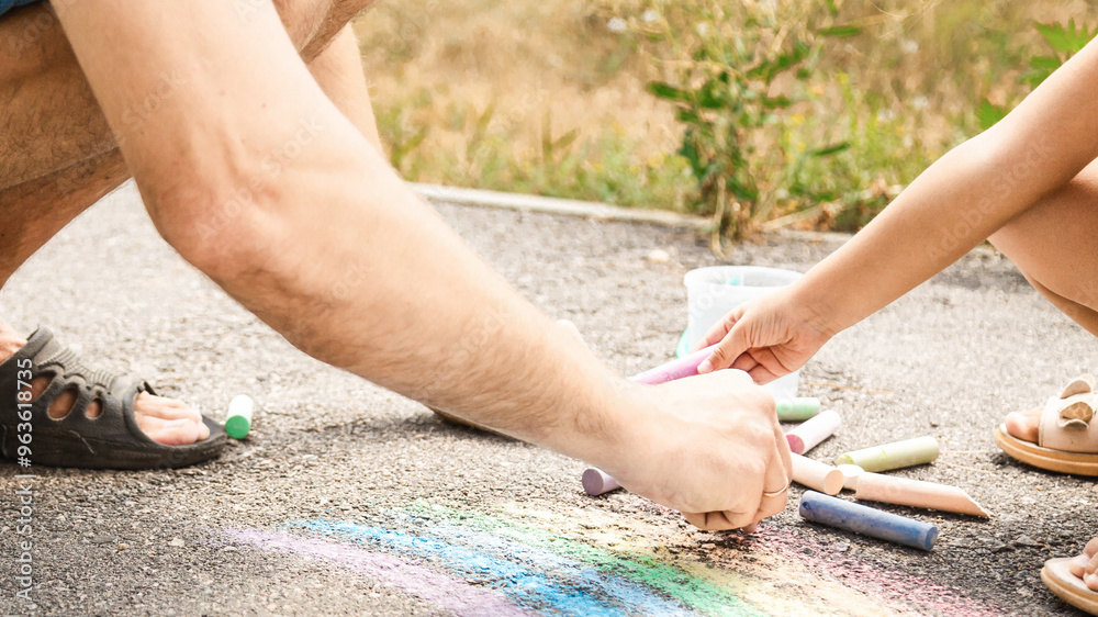 Father and his little daughter drawing together with chalks on street in summer Father and his little daughter drawing together with chalks on street in summer