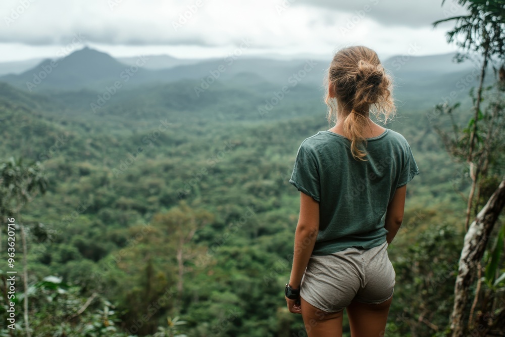 Woman enjoys a breathtaking forest view from a mountaintop on a cloudy day Woman enjoys a breathtaking forest view from a mountaintop on a cloudy day
