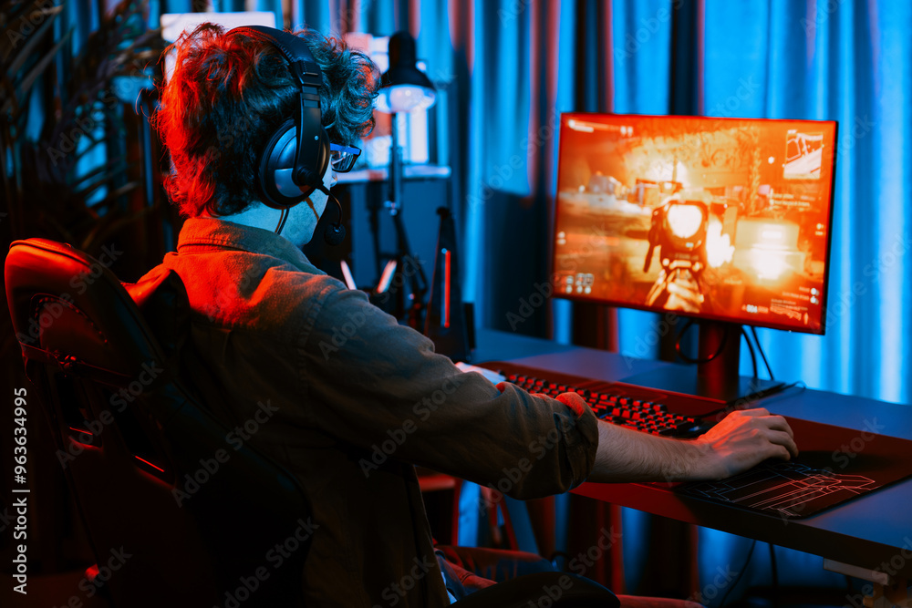 Host channel of young gaming streamer, team gamer playing battle game shooting with multiplayer at warship on pc screen with back side image, wearing headset with mic at digital neon room. Gusher. Host channel of young gaming streamer, team gamer playing battle game shooting with multiplayer at warship on pc screen with back side image, wearing headset with mic at digital neon room. Gusher.