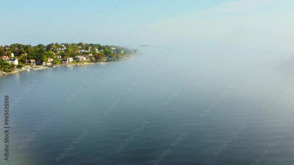 Morning fog rolling over an island in early autumn, Dalarö, Swedish archipelago, Sweden. Bright summer houses, trees, boats. Blue sky, bright sunlight Morning fog rolling over an island in early autumn, Dalarö, Swedish archipelago, Sweden. Bright summer houses, trees, boats. Blue sky, bright sunlight