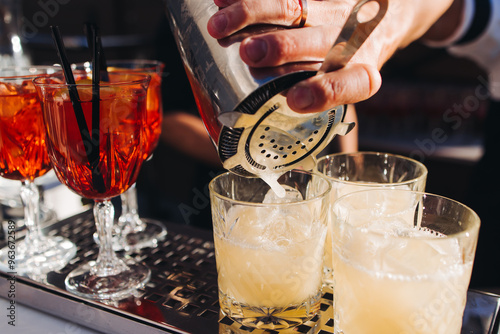 Bartender working, beautiful row line of different coloured liquor alcohol cocktails on a open air party in a bar, and others on catering banquet on event, barman mixing drinks and beverages in club
