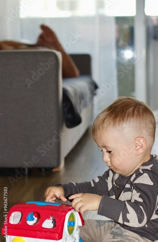 The baby plays alone on the floor with a toy house while the adults rest