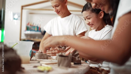 Handsome student dipping hand in to water to soften clay at art classroom. Group of diverse children working or modeling vase. Happy boy put water to young girl while laugh with happy. Edification photo