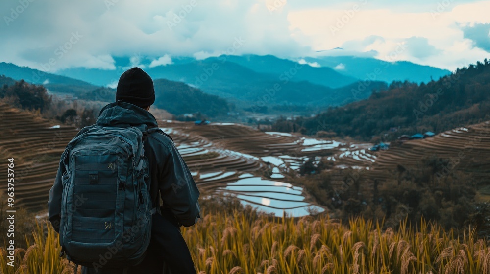 A lone traveler with a backpack stands on a mountain overlooking rice terraces. A lone traveler with a backpack stands on a mountain overlooking rice terraces.