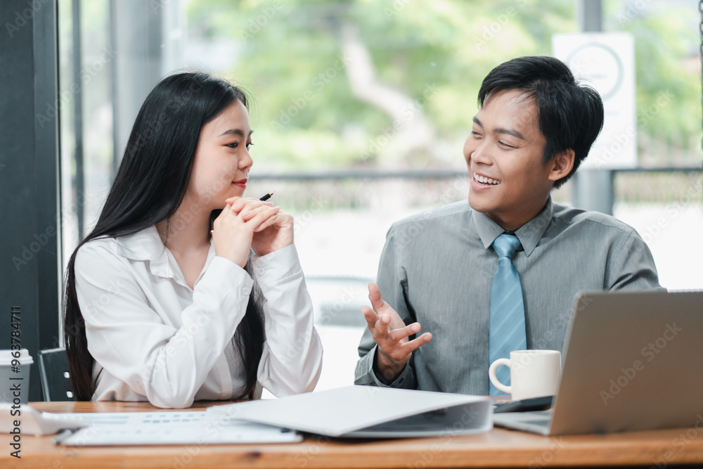 Two business colleagues having a discussion in a modern office setting with natural light and greenery visible outside. Two business colleagues having a discussion in a modern office setting with natural light and greenery visible outside.