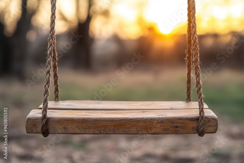 Wooden swing hanging from ropes in a serene outdoor setting with a warm sunset in the background. Idyllic and nostalgic scene. photo