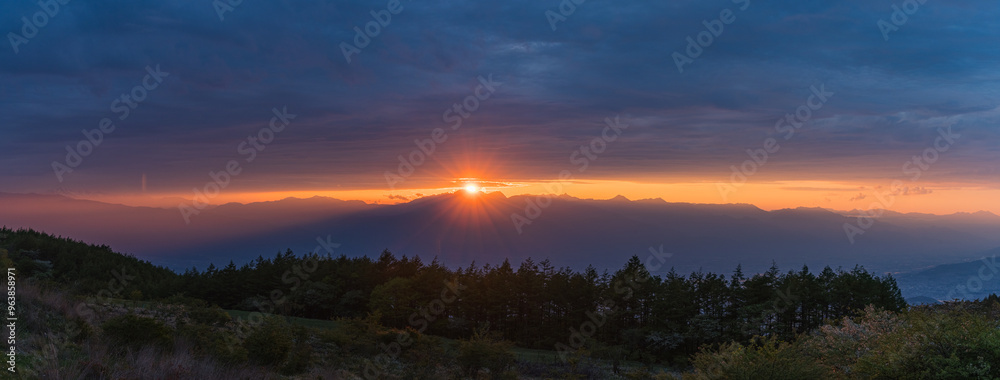Fototapeta premium 日本 長野県岡谷市と塩尻市の境にある高ボッチ山の高ボッチ高原から見える夕陽の光芒と雲から顔を出した夕日