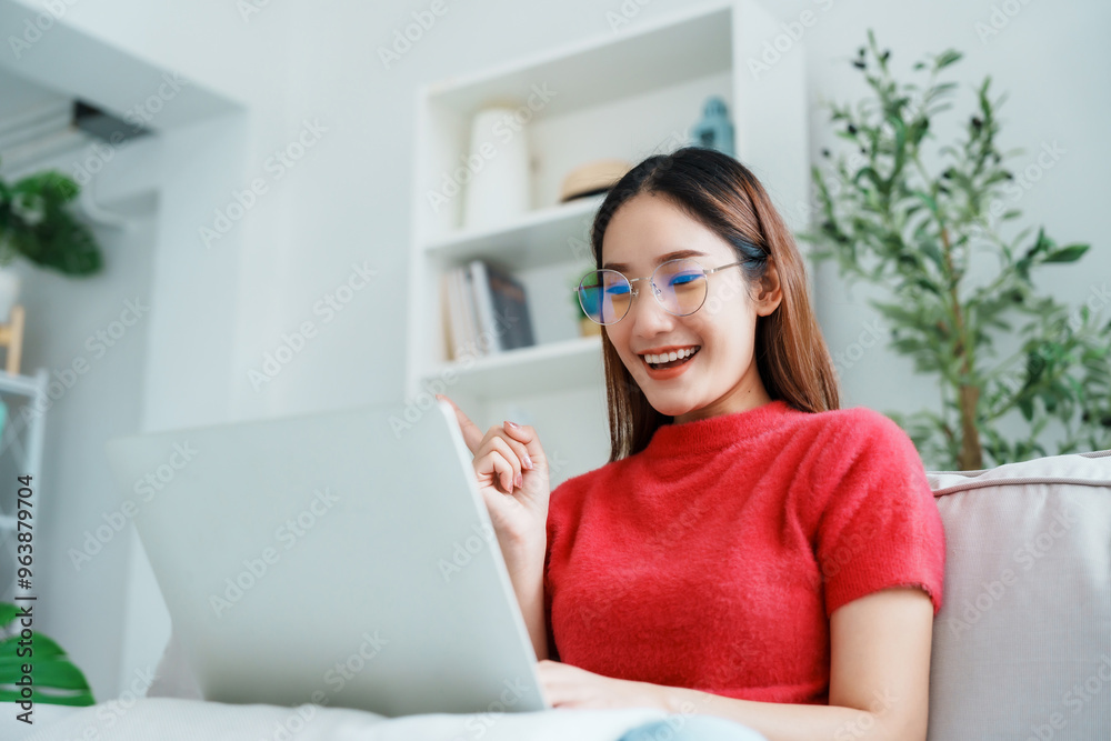 Happy young Asian woman using laptop while seated on couch at home Happy young Asian woman using laptop while seated on couch at home
