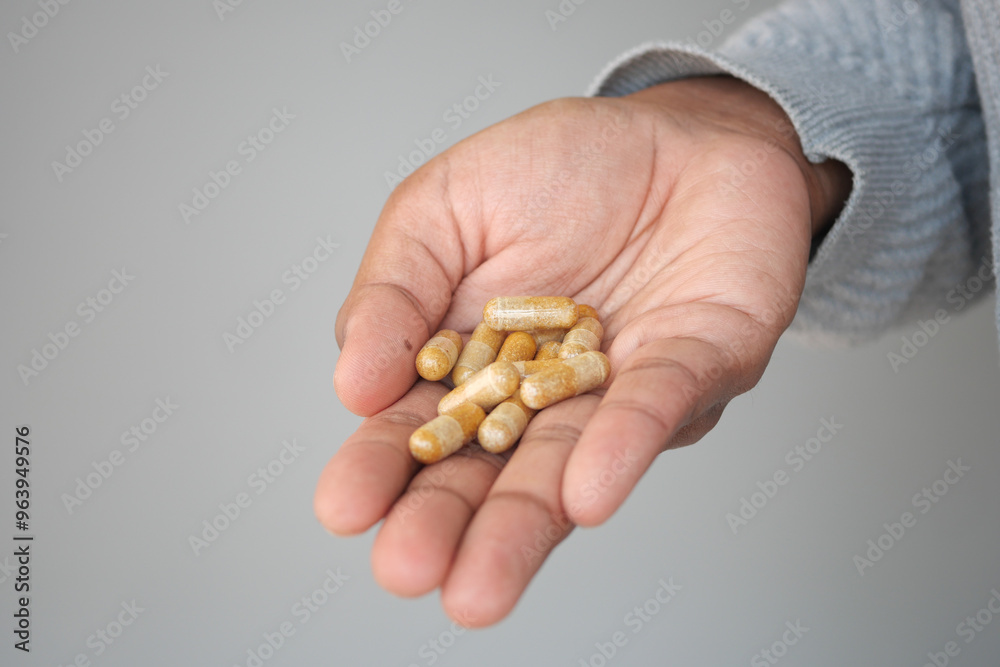 Close up of man hand holding capsule against orange background Close up of man hand holding capsule against orange background