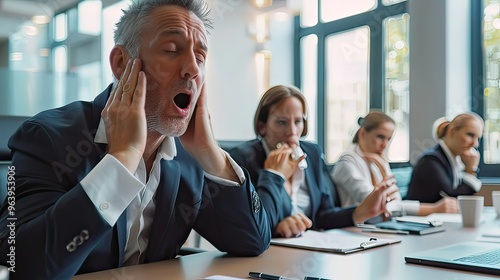 Middle-aged white business professional stifling a yawn while listening to a presentation in a boardroom.  photo