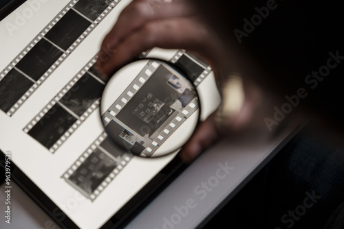 Close-up of a person's hand analyzing film negatives on a lightbox using a magnifying glass to inspect details. photo
