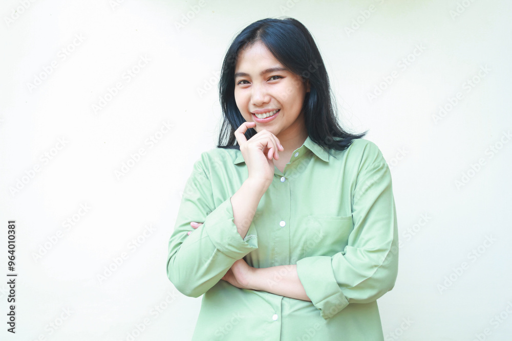 image of pleased curious asian woman wearing green over size shirt looking at camera with hands on chin arms folded standing over isolated white background with wonder face expression image of pleased curious asian woman wearing green over size shirt looking at camera with hands on chin arms folded standing over isolated white background with wonder face expression