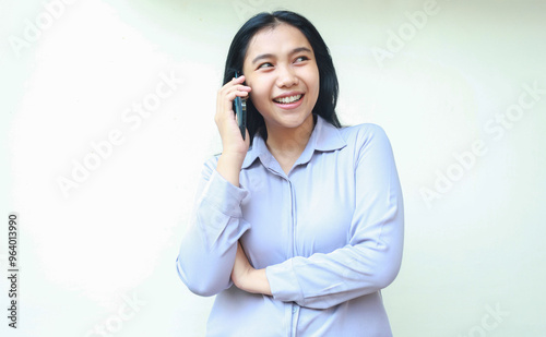 smiling asian young business woman excited to make a call to talking on cell phone looking away with folded arm wear formal shirt isolated on white background