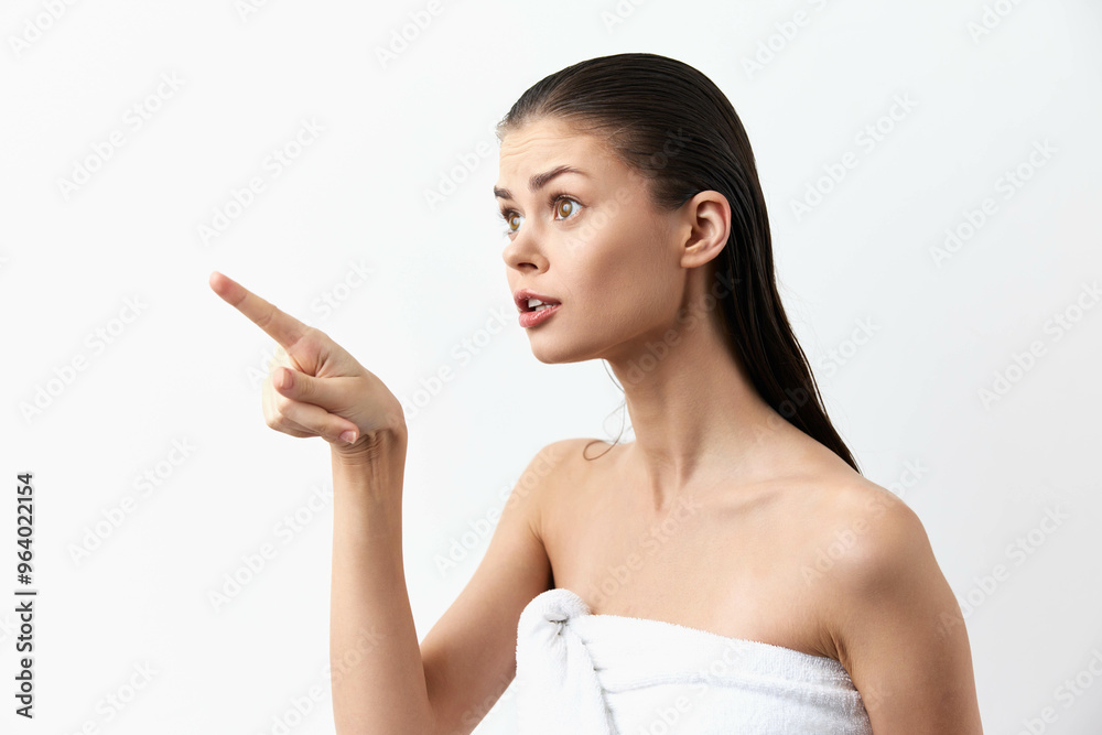 Young woman pointing with an expression of surprise against a white background, with wet hair and a towel, conveying a moment of realization or communication Young woman pointing with an expression of surprise against a white background, with wet hair and a towel, conveying a moment of realization or communication