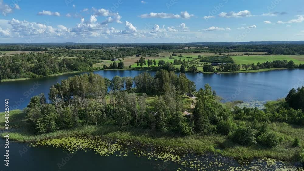 Aerial view of lakes and forest landscape in Lithuania on a sunny day. Drone view of serene lakes surrounded by green forests and fields under a clear blue sky in Lithuania.