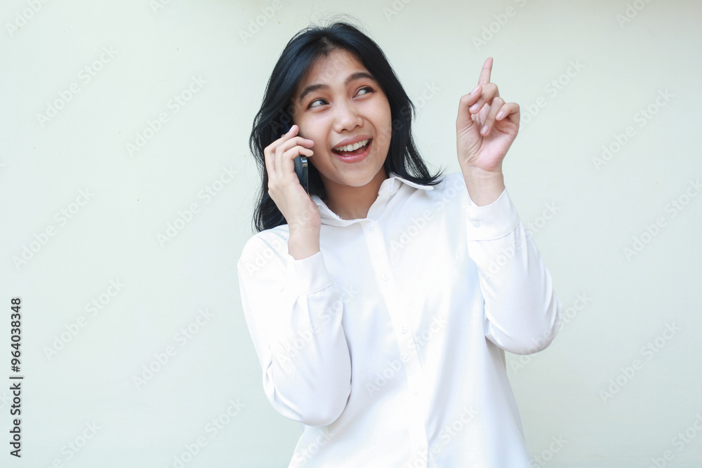 portrait pleased asian young woman secretary pointing finger up looking above to empty space while speaking on mobile phone wearing white formal suit shirt, wireless conversation, standing isolated portrait pleased asian young woman secretary pointing finger up looking above to empty space while speaking on mobile phone wearing white formal suit shirt, wireless conversation, standing isolated
