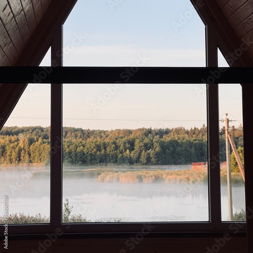 view of the lake early in the morning in light fog in summer from an A frame tourist house through the window photo