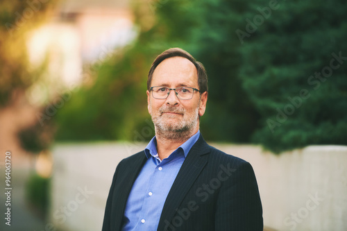 Outdoor portrait of handsome middle age man wearing suit, posing in sunlight