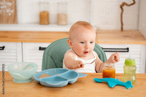 a baby boy eats baby puree in a high chair, a small child eats on his own with a spoon, baby food